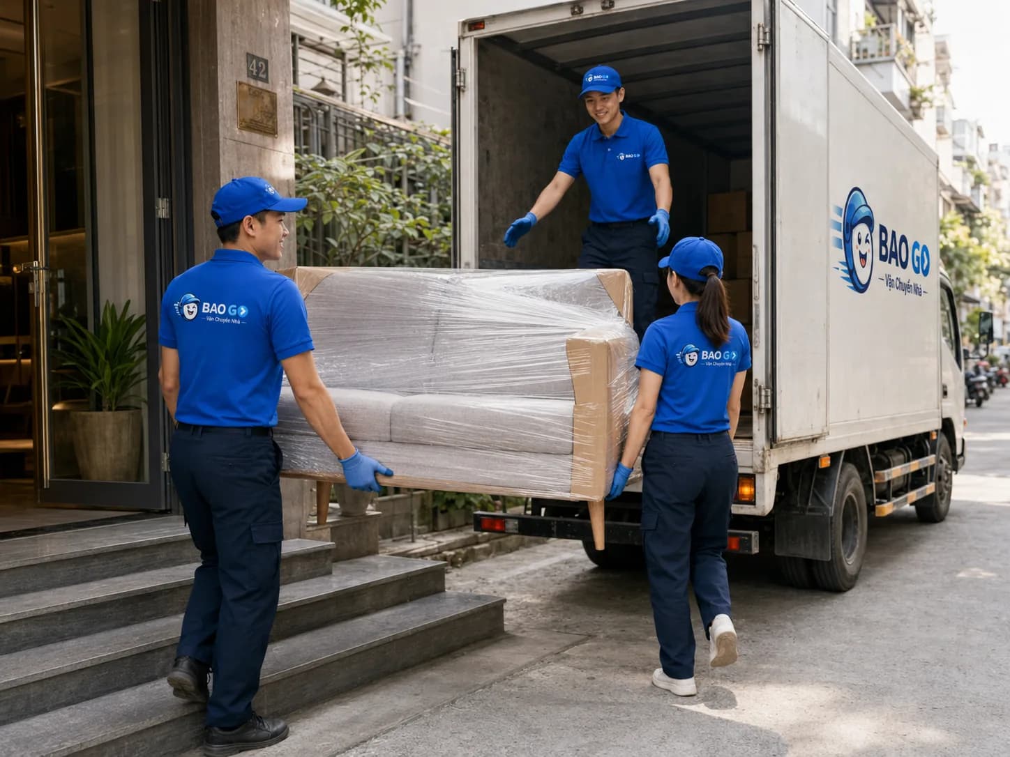 Hai thợ BAO GO khiêng sofa đã bọc màng PE lên xe